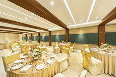 a banquet room set up with round tables and white linens, gold chairs and yellow sashes