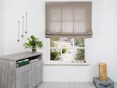 a white room with a window and a cabinet in it, next to a potted plant