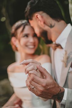 a bride and groom holding hands while looking at their wedding ring in front of them