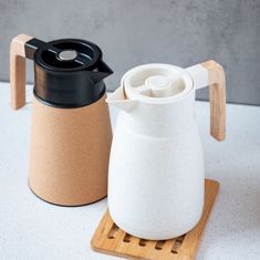 two coffee mugs sitting next to each other on a wooden coaster with a black lid