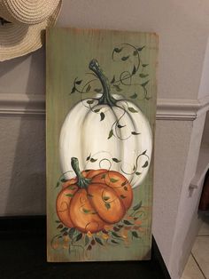 a painting of a white pumpkin with leaves on it sitting on a shelf next to a straw hat