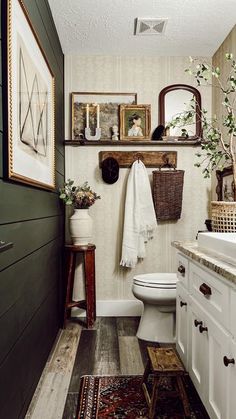 a white toilet sitting in a bathroom next to a wooden cabinet and counter with pictures on the wall