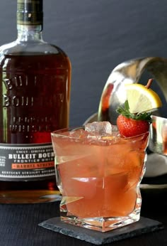 a bottle of booze next to a glass with a strawberry on the rim and a strawberries garnish