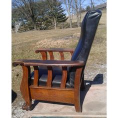 a wooden chair with black leather seat and back rests on concrete in front of grassy area