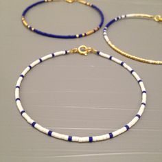 three bracelets with blue, white and gold beads on a gray table next to each other