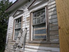 an old ladder leaning against the side of a house with broken windows and siding on it