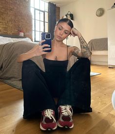 a woman sitting on the floor with her cell phone in her hand and wearing red sneakers