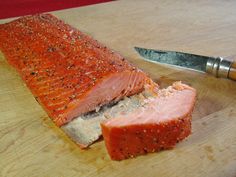 a piece of salmon on a cutting board next to a knife and peppercorst