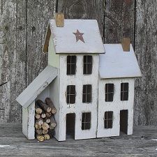 a small white house sitting on top of a wooden table next to a pile of logs