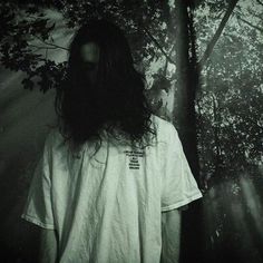 a man with long hair standing in front of trees