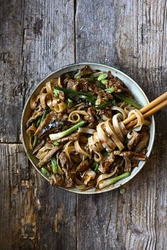 a bowl filled with noodles and meat next to chopsticks on top of a wooden table