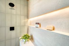 a bathroom with a white tiled wall and bathtub next to a green potted plant