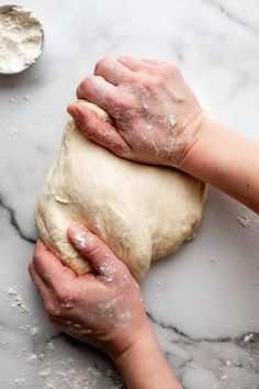 two hands kneading dough on top of a marble counter with powdered sugar