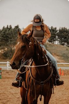 a woman riding on the back of a brown horse across a dirt field with trees in the background