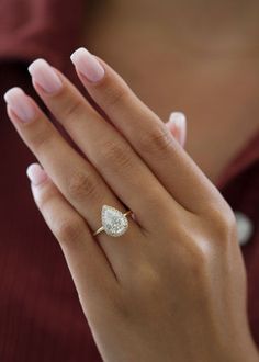 a woman's hand with a diamond ring on her left hand, wearing a maroon shirt