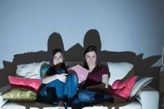 two women sitting on a couch with their arms around each other and pillows in front of them