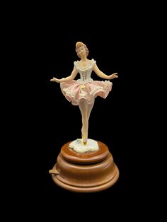 a figurine of a ballerina on top of a wooden base with her arms outstretched