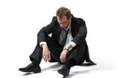 a man in a suit and tie sitting on the ground with his hands clasped to his knees