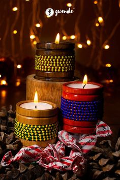 three candles sitting on top of each other in front of some pine cones and lights