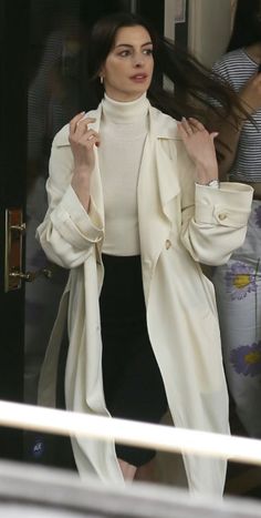 a woman in white jacket and black skirt walking out of a building with her hair blowing