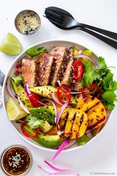 a white bowl filled with meat and veggies next to some dipping sauces