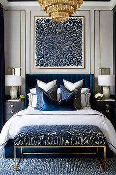 a bedroom with blue and white bedding, chandelier and artwork on the wall