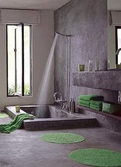 a bathroom with a tub, shower head and green rugs on the floor in front of two windows