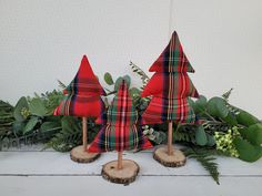 three red plaid christmas trees sitting on top of a wooden table next to greenery