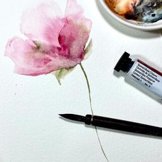 a pink flower sitting on top of a white table next to a cup of coffee