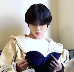 a woman reading a book while sitting at a table in front of a glass bottle