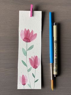 a watercolor painting of pink flowers next to a blue pen on a wooden table