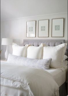 a bed with white linens and pillows in a bedroom next to two pictures on the wall