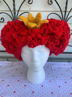 a crocheted red hat with yellow flowers on top sits on a white mannequin head