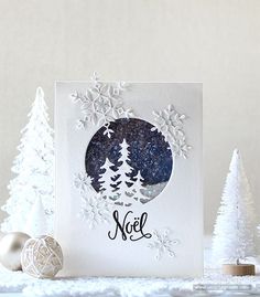 a card with snowflakes and trees on it, next to some ornaments in the background