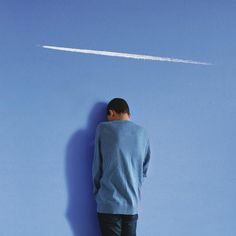 a man standing in front of a blue wall looking at an airplane flying through the sky