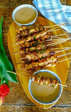 several skewers of food sitting on a wooden platter with dipping sauces