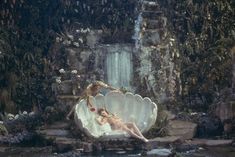 a woman laying on top of a large shell next to a waterfall in a forest