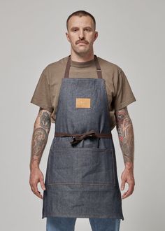 a man wearing an apron with tattoos on his arm and chest, standing in front of a gray background