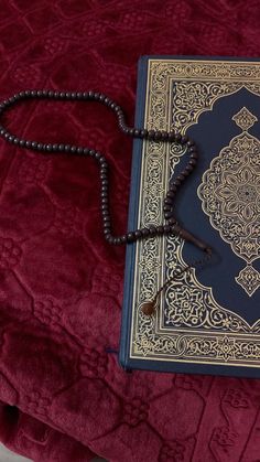 a book with a rosary on top of it sitting on a red velvet bed spread