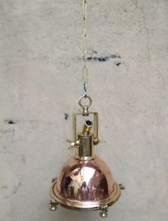 a small bell hanging from a chain on a concrete wall with a light fixture attached to it