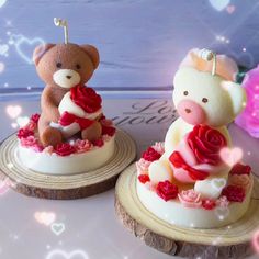 two small teddy bears sitting on top of wooden slices covered in frosting and roses