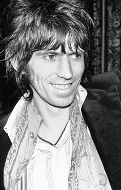 a black and white photo of a man with long hair wearing a jacket smiling at the camera