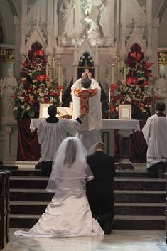 the bride and groom are sitting at the alter in front of the priest who is kneeling down