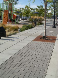 an empty sidewalk next to a park with children's playgrounds in the background