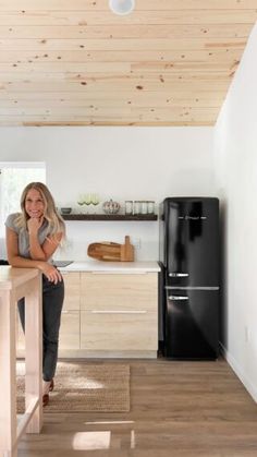 a woman standing at the counter in a kitchen with wood floors and white walls, looking into the camera