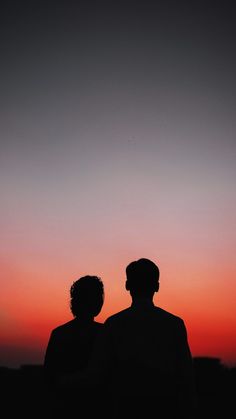 two people standing in front of a sunset