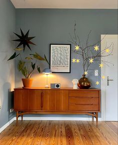 a living room with wooden floors and plants on top of the entertainment center, in front of a white door