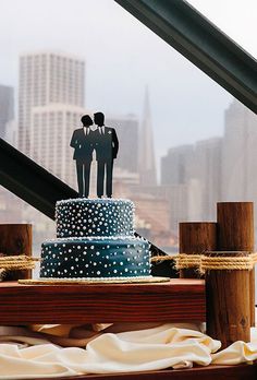 a wedding cake with two people on top is displayed in front of a cityscape