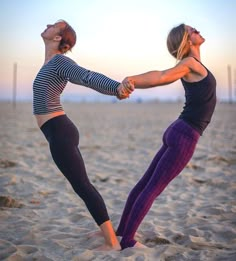 two women doing yoga poses on the beach at sunset with their hands in each other's pockets