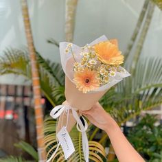 a hand holding a bouquet of flowers in front of palm trees and other tropical plants